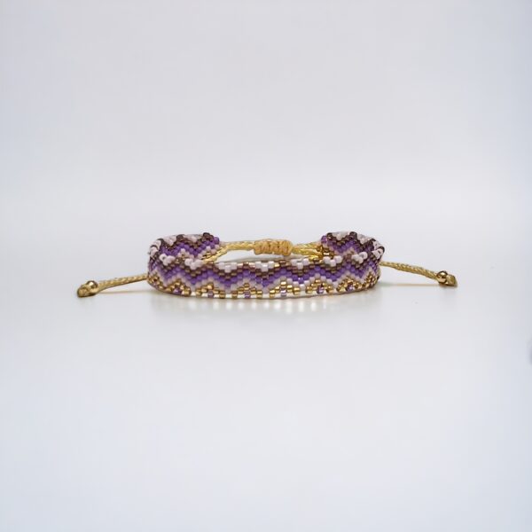 Purple beaded bracelet with gold accents on white background.